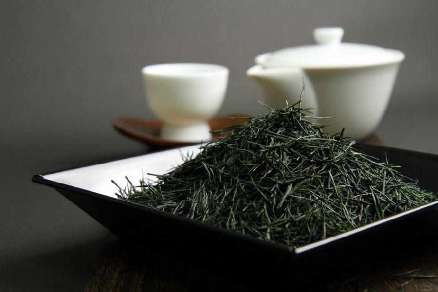 Earth's Gyokuro leaves piled on a black dish beside a white kyusu and cups