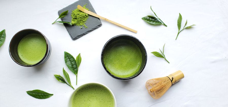 Bowls of whisked matcha with a bamboo whisk and fresh tea leaves